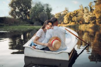 Love couple in boat on quiet lake at summer day. Romantic date, boating trip, man and woman walking along the river
