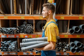 Male builder choosing piping at the shelf in hardware store. Constructor in uniform look at the goods in diy shop