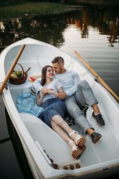 Love couple lying in a boat on quiet lake and dreaming at sunset. Romantic meeting, boating trip, man and woman walking along the river