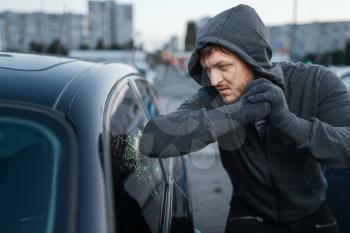Car thief breaking door glass, criminal job, burglar. Hooded male robber opening vehicle on parking. Auto robbery, automobile crime, vandalism