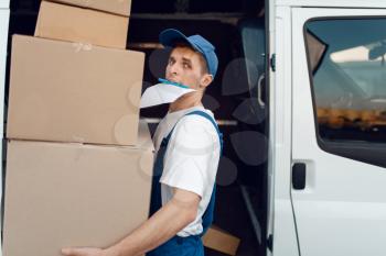 Loader in uniform holding stack of parcels, delivery service. Man standing at cardboard packages in vehicle, male deliver, courier or shipping job