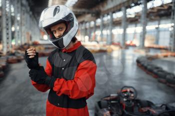 Kart racer in red uniform, helmet and gloves, karting auto sport indoor. Speed race on close go-kart track with tire barrier. Fast vehicle competition, high adrenaline hobby