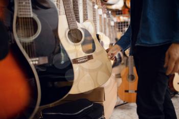 Male customer choosing acoustic guitar in music store. Assortment in musical instruments shop, musician buying equipment
