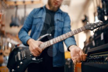 Male guitarist plays on electric guitar in music store. Assortment in musical instruments shop, musician buying equipment