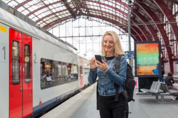 Female tourist with phone waiting for the train on railway station platform, travel in Europe. Transportation by european railroads, comfortable tourism and travelling