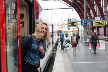 Female tourist looks out of the train on railway station platform, travel in Europe. Transportation by european railroads, comfortable tourism