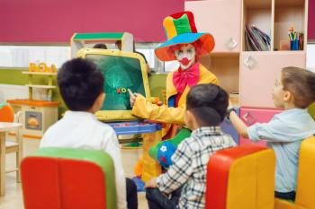 Funny clown with happy children play in the alphabet on board. Birthday party celebrating in playroom, baby holiday in playground. Childhood happiness, childish leisure