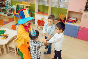 Funny clown with cheerful children play counting game together. Birthday party celebrating in playroom, baby holiday in playground. Childhood happiness, childish leisure