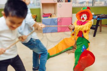 Funny clown and joyful little boys playing tug of war together. Birthday party celebrating in playroom, baby holiday in playground. Childhood happiness, childish leisure
