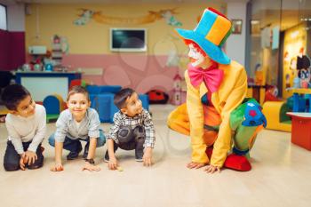 Funny clown animator play with group of little boys. Birthday celebrating in playroom, baby holiday in playground. Childhood happiness, childish leisure, entertainment in children's area
