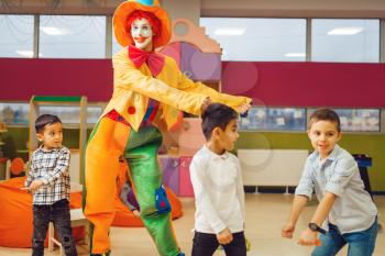 Funny clown animator dancing with little boys in kindergarten. Birthday celebrating in playroom, baby holiday in playground. Childhood happiness, childish leisure, entertainment in children's area