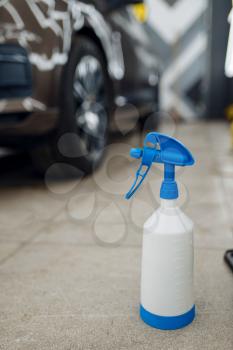 Bottle with spray gun, car with protection film on background, nobody. Installation of coating that protects the paint of automobile from scratches. New vehicle in garage, auto tuning