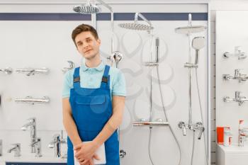 Plumber in uniform at showcase with boilers in plumbering store. Man with notebook buying sanitary engineering in shop, water taps and faucets choice