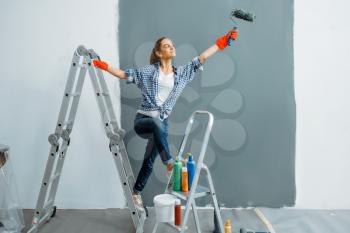 Cheerful female house painter paints walls indoor. Home repair, laughing woman doing appartment renovation, room decoration renovating