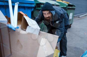 Bearded homeless searching food in trashcan on city street. Poverty is a social problem, homelessness and loneliness, alcoholism and drunk addiction, urban lonely
