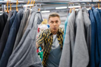 Young man choosing bathrobe in bed linen store. Male person buying home goods in market, guy in bedding shop