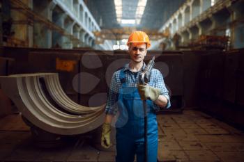 Male worker in uniform and helmet holds pneumatic jackhammer on factory. Metalworking industry, industrial manufacturing of steel products