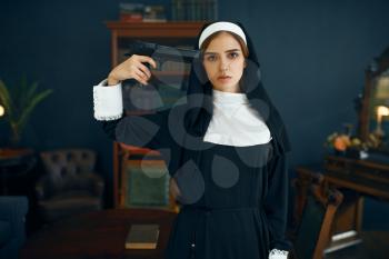 Young nun in a cassock with a gun at her temple, vicious desires, the sin of suicide. Corrupt sister in the monastery, religion and faith, sinful religious people, attractive sinner