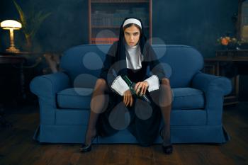 Sexy nun in a cassock with cigare and glass of wine sitting spreading her legs, front view, vicious desires. Corrupt sister in the monastery, sinful religious people, attractive sinner