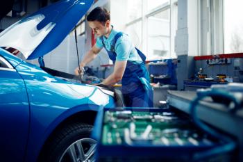 Worker in uniform checks vehicle engine, car service station. Automobile checking and inspection, professional diagnostics and repair
