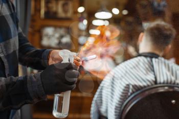 Barber processes the blade with fire, customer sitting in chair. Professional barbershop is a trendy occupation. Male hairdresser and client in hair salon