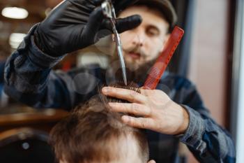 Barber with comb and scissors makes stylish haircut to a client. Professional barbershop is a trendy occupation. Male hairdresser and customer in retro style hair salon