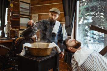 Barber soaks the towel, beard cutting. Professional barbershop is a trendy occupation. Male hairdresser and client in hair salon