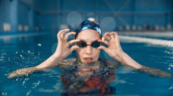 Female swimmer in swimsuit, swimming cap and glasses poses in pool. The woman at the poolside, aqua aerobics training, healthy lifestyle