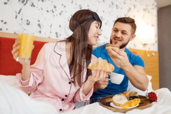 Romantic love couple, breakfast in bed at home, good morning, caring husband. Harmonious relationship in young family. Man and woman resting together in their house, carefree weekend
