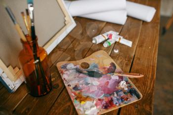 Paints on palette, brush in bottle, canvas, nobody. Painter tools on the table in art studio, equipment on artist workplace, paintbrush, creative atelier or workshop