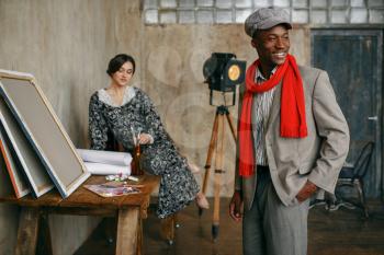 Portrait painter in a red scarf and female model in art studio. Male artist standing at his workplace, creative master in workshop