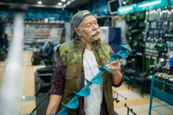 Fisherman holds a drill for winter fishing in shop. Male angler buying equipment and tools for fish catching and hunting, assortment on showcase in store