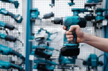 Male worker hand holds electric drill in tool store. Choice of professional equipment in hardware shop, electrical instrument supermarket