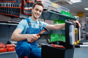 Happy male worker in uniform choosing toolbox in tool store. Choice of professional equipment in hardware shop, instrument supermarket