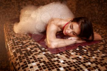 Woman in foam lying on a hot stone, turkish bath, hamam, sauna, top view. Skin and body care