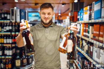 Cheerful man choosing alcohol in grocery store. Male person buying beverages in market, customer shopping food and drinks