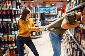 Funny couple choosing alcohol in grocery store. Man and woman with cart buying beverages in market, customers shopping food and drinks