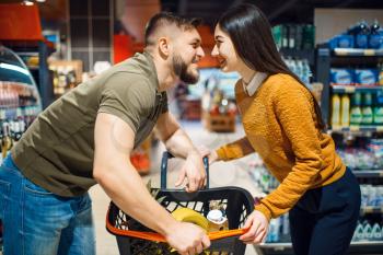 Love couple poses in grocery store. Man and woman with cart buying beverages and products in market, customers shopping food and drinks