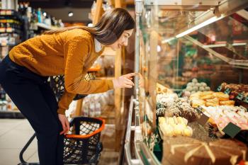 Young woman choosing cakes in grocery store, sweets department. Female person buying fruits and vegetables in market, customer shopping food