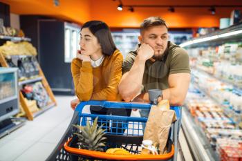 Bored family couple in grocery store. Man and woman with cart buying beverages and products in market, two customers shopping food and drinks