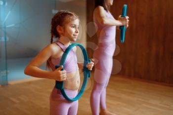 Mother and daughter in gym, pilates exercise with rings, yoga workout. Mom and little girl in sportswear, woman with kid on joint training in sport club