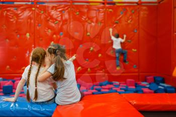 Children plays on climbing wall in the entertainment center. Girls and boy leisures on holidays, childhood happiness, happy kids on playground