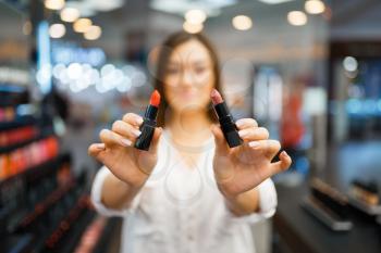 Woman shows two lipsticks in cosmetics store. Buyer at the showcase in luxury beauty shop salon, female customer in fashion market