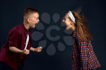 Little boy and girl are shouting at each other in studio, developing hair effect. Children and wind, kids isolated on dark background, child emotion