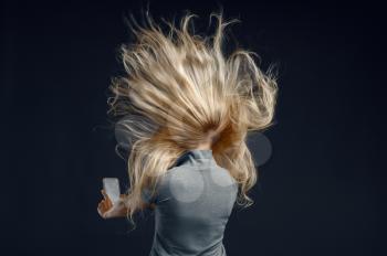 Woman standing against powerful airflow in studio, back view, developing hairstyle effect. Female person and wind, lady isolated on dark background