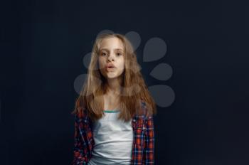 Schoolgirl makes face leaning against the glass in studio. Happy childhood, children having fun, funny kid isolated on dark background, child emotion