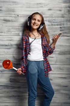 Little girl in headphones holds big lollipop in studio. Children and gadget, kid isolated on wooden background, child emotion, schoolgirl photo session