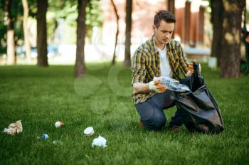 Young man collects garbage in a bag in park, volunteering. Male person cleans forest, ecological restoration, eco lifestyle, trash collection and recycling, ecology care, environment cleaning