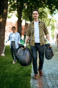Young man holds plastic trash bags in park, volunteering. Male person cleans forest, ecological restoration, eco lifestyle, garbage collection and recycling, ecology care, environment cleaning