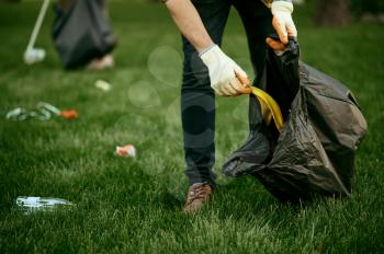 Young man collects garbage in a bag in park, volunteering. Male person cleans forest, ecological restoration, eco lifestyle, trash collection and recycling, ecology care